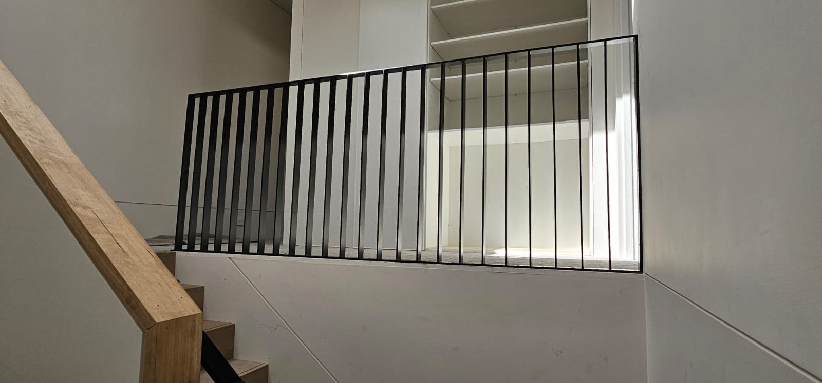 Slim black vertical steel balustrade beside timber stairs and white interior walls