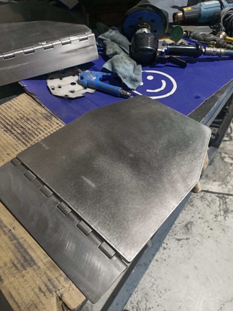 Pair of shaped metal trim plates with continuous hinges on a workshop bench