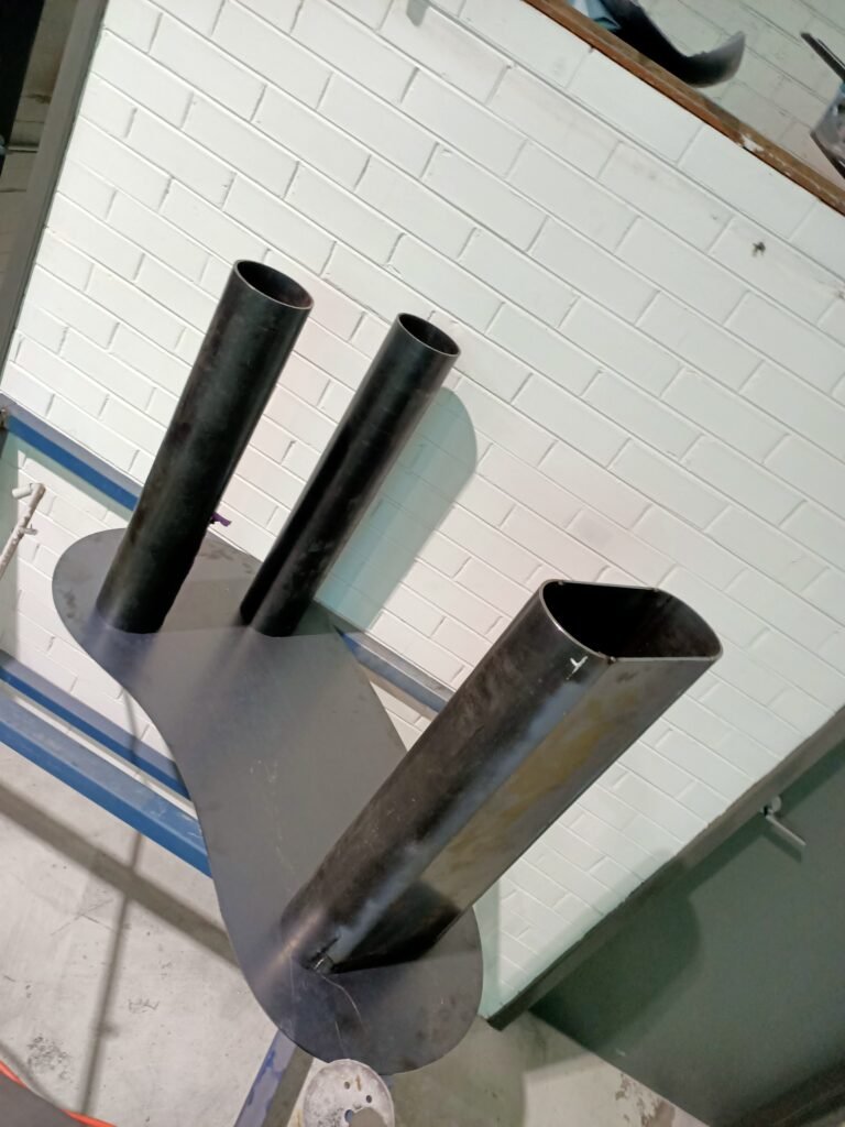 Underside of a curved metal table with three tubular legs during fabrication