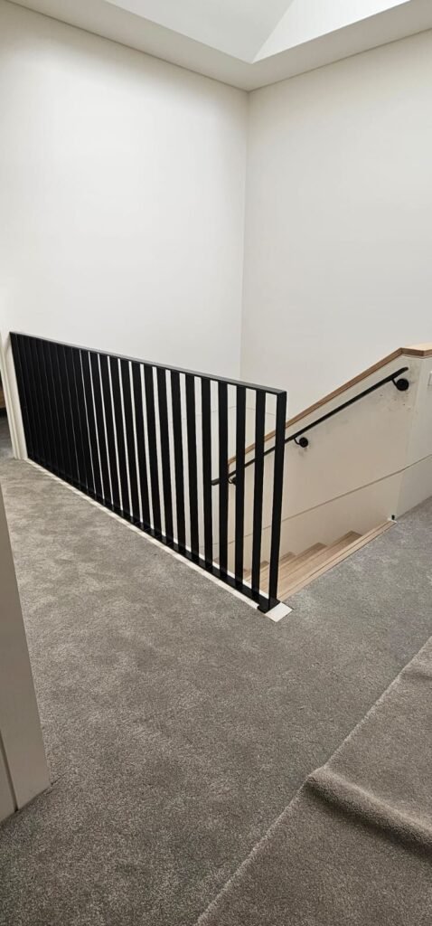 Black vertical balustrade and wall-mounted handrail at an interior stair landing